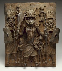 169. Wall plaque, from Oba's Palace
Location: Benin Kingdom (near Nigeria)
Artist: Edo peoples
Date: 16th century C.E.
Culture: Benin
Period/Style: 16th Century Benin
Medium/Material: Cast brass
Theme(s): Royalty, ceremony, authority
Form: hierarchy of scale to show importance of figures in the plaque. medium-deep relief. 
Function: to depict an Oba and his attendants 
Content: central figure is an Oba because of his distinctive coral beaded regalia. Attendants hold shields above his head either to protect him from attack or possibly from the sun; a privilege only afforded to an Oba. 
Context: The plaque originally hung alongside many others on posts throughout the palace of the Oba. The order of their placement on these posts would have told the history of the royal lineage of Benin's Obas, who traced their dynasty all the way back to Oranmiyan, whose son was the first Oba of Benin.
