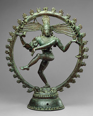 Shiva as Lord of Dance 

Hindu, India, Chola Dynasty, 11th century, Cast bronze

Vigorously dancing with one foot on dwarf, Demon of Ignorance, often depicted in a flaming nimbus
flying locks of hair terminate in rearing cobra hands
one hand sounds the drum that he dances to another has a flame
Ring of fire surrounding him is the encapsulated universe with endless cycle of periodically destroying the universe so it can be reborn again, moves in tune with the dance
Lower right hand in gesture saying not to be afraid 
unfolds universe out of the drum held in one of his right hands, 
Shiva has a third vertical eye suggested between his two other eyes
Face stays tranquil despite scene of chaos